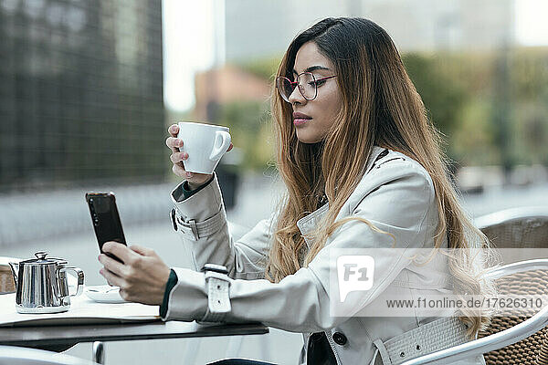 Woman holding coffee cup using smart phone at sidewalk cafe