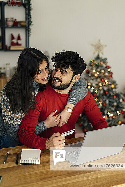 Woman embracing boyfriend shopping online through laptop at home