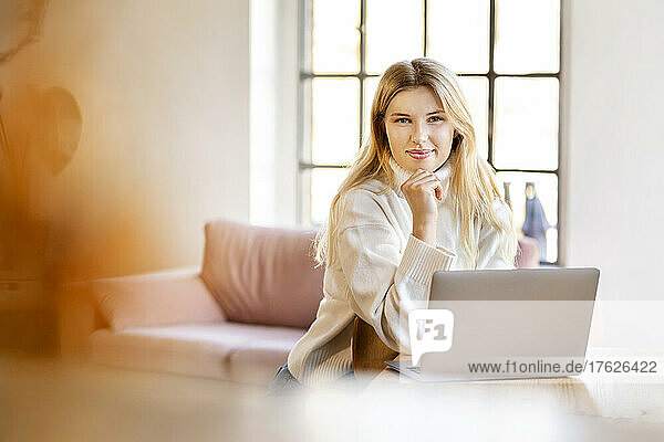 Smiling blond businesswoman sitting with laptop at home