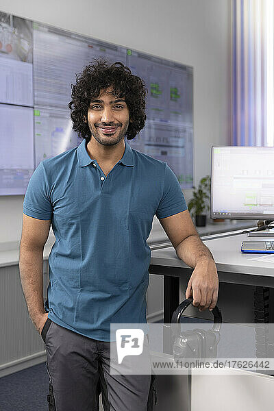 Smiling technician standing with hand in pocket at desk