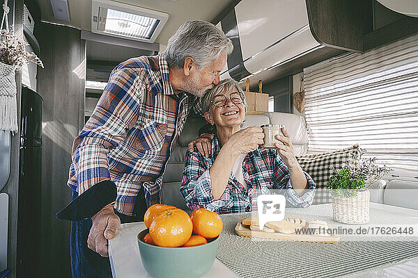 Senior man kissing happy woman in motor home at vacation
