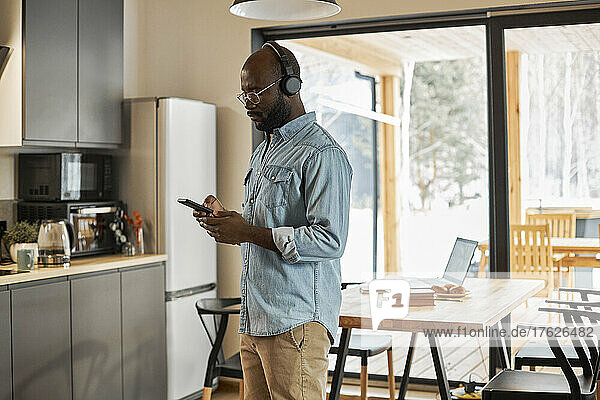 Man using smart phone standing in kitchen at home