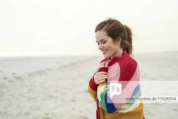 Happy young woman wearing multi colored sweater standing on beach