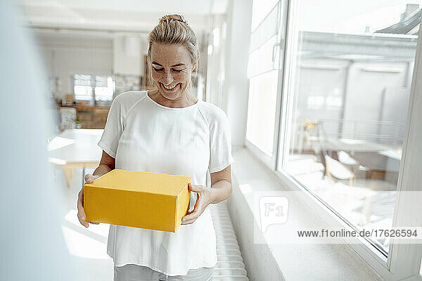 Cheerful businesswoman standing with box in office