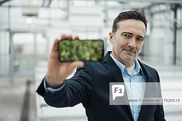 Businessman showing mobile phone device screen in greenhouse