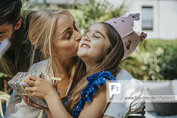 Mother kissing daughter with gift celebrating her birthday