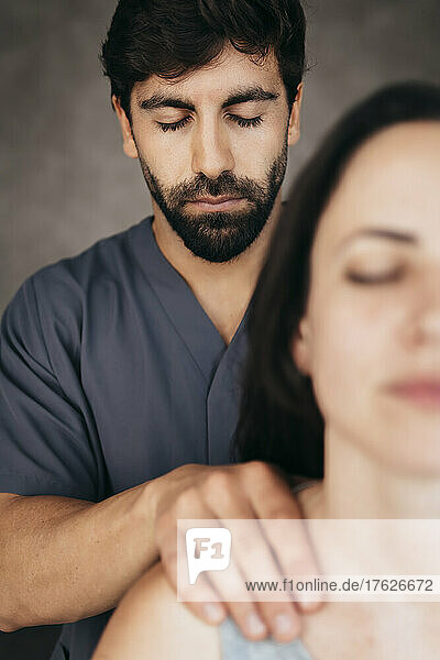 Physiotherapist with eyes closed giving massage on shoulder to woman