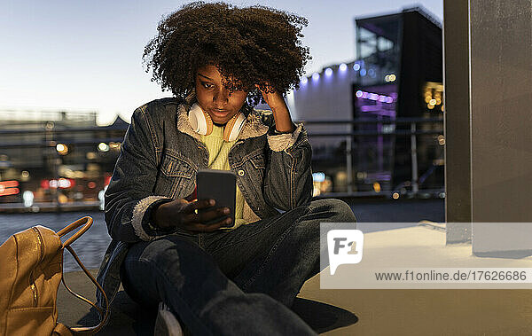 Young woman with headphones using mobile phone at night