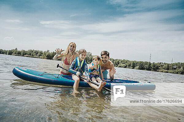 Cheerful family with paddleboard in lake on weekend