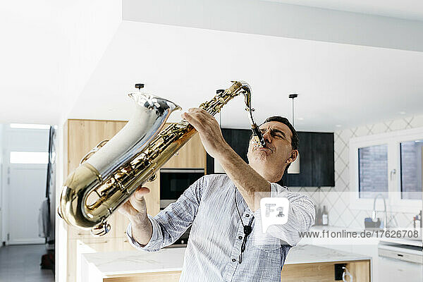 Passionate saxophonist practicing saxophone in kitchen at home
