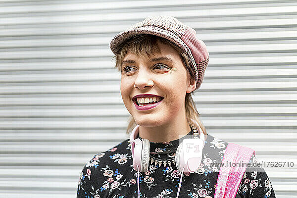 Happy young woman with flat cap standing in front of closed shutter