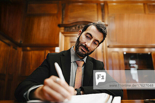 Confident bearded male lawyer signing contract document in board room during meeting