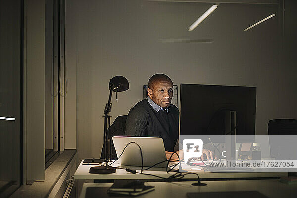 Dedicated businessman using computer while working overtime in office at night
