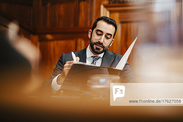 Confident bearded businessman with contract file sitting in board room during meeting