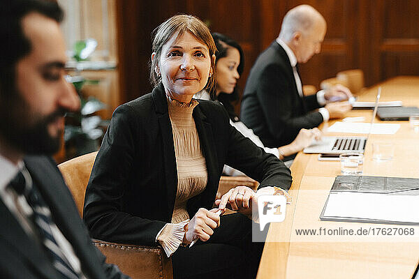 Portrait of smiling female lawyer in board room with colleagues during meeting