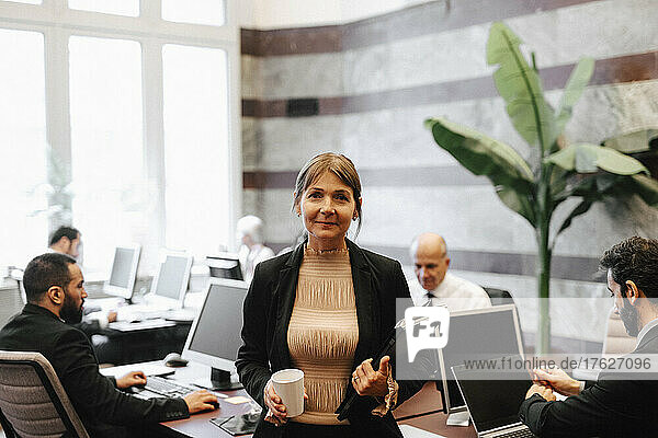 Porträt einer lächelnden reifen weiblichen Führungskraft mit Kaffeetasse und Dokumenten in einer Anwaltskanzlei