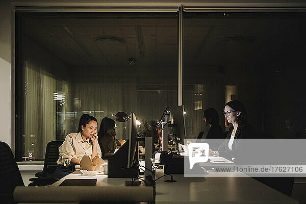 Multiracial female colleagues working late night at desk in office