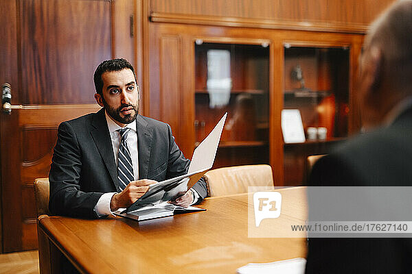 Confident male financial advisor discussing contract with senior businessman in board room