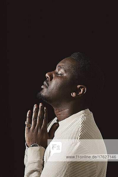 Seitenansicht eines Mannes mit verschränkten Händen vor schwarzem Hintergrund