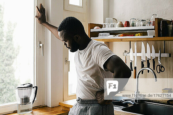 Depressiver einsamer Mann mit Hand auf der Hüfte in der Küche zu Hause stehend