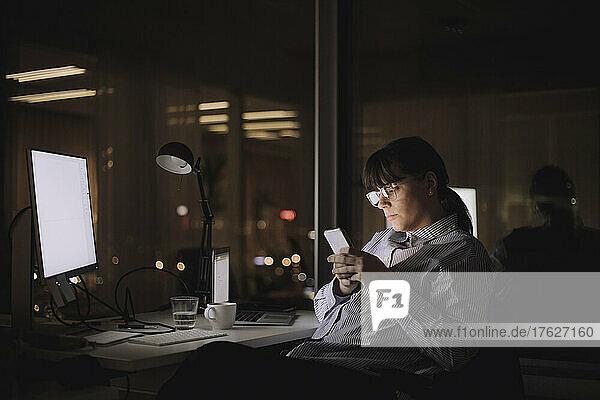 Geschäftsfrau Textnachrichten auf Smartphone sitzend am Arbeitsplatz