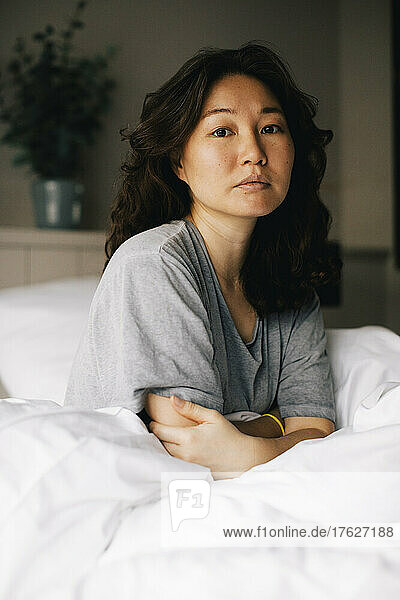 Porträt einer einsamen Frau  die zu Hause auf einem Bett mit weißer Decke sitzt