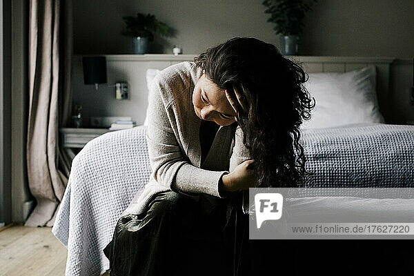 Emotional depressive Frau sitzt mit der Hand im Haar auf dem Bett zu Hause
