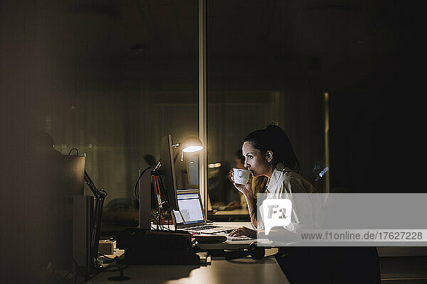 Businesswoman drinking coffee while working overtime in office at night