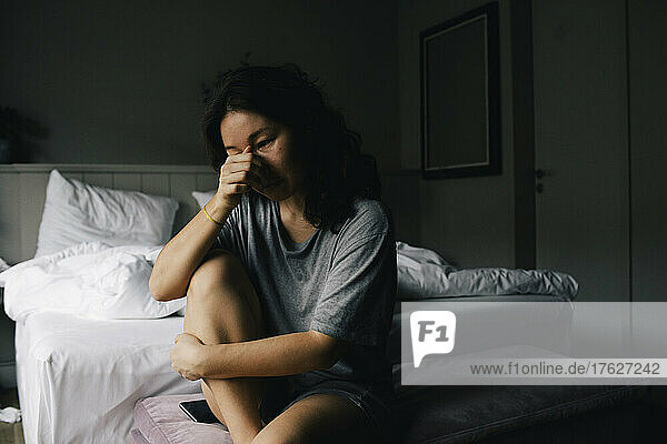 Traurige Frau weint  während sie auf der Bank am Bettende im Schlafzimmer zu Hause sitzt