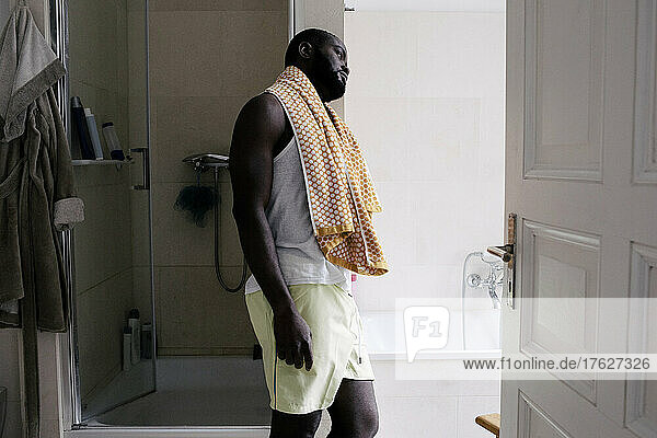 Geistig erschöpfter Mann mit Handtuch  das zu Hause an der Badezimmerwand lehnt