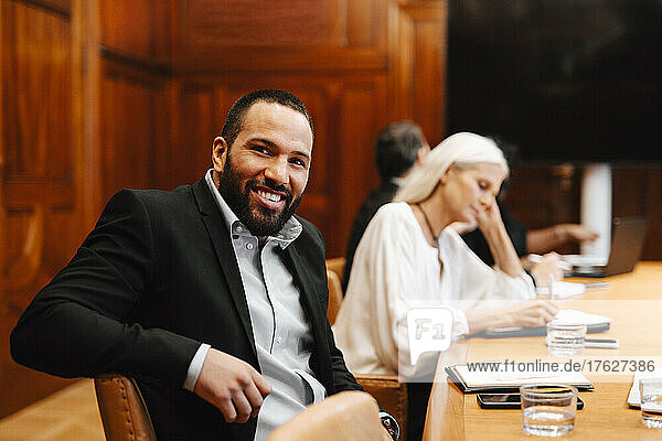 Porträt eines lächelnden Geschäftsmannes  der während einer Sitzung am Konferenztisch im Sitzungssaal sitzt
