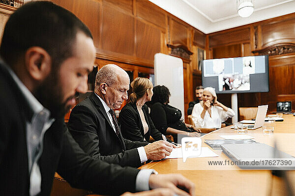 Männlicher Finanzberater bei der Unterzeichnung eines Vertrags während einer Sitzung mit Kollegen im Sitzungssaal