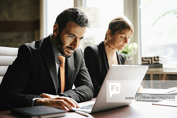 Geschäftsmann mit Laptop  der neben einer Geschäftsfrau am Schreibtisch in einer Anwaltskanzlei arbeitet