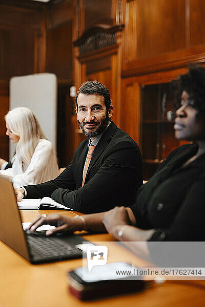 Portrait of confident businessman sitting with female colleagues in board room during conference meeting