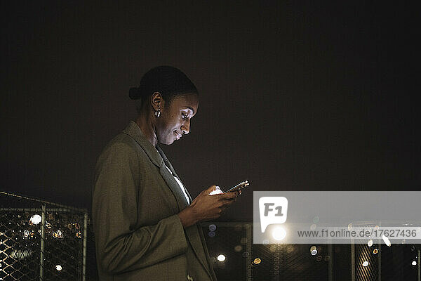 Seitenansicht einer Geschäftsfrau  die nachts eine Textnachricht auf einem Mobiltelefon schreibt