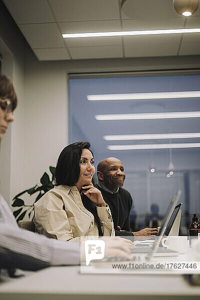 Smiling businesswoman with male and female colleagues discussing while working late at office