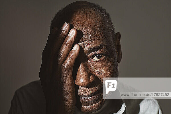 Älterer Mann bedeckt Auge mit Hand über weißem Hintergrund