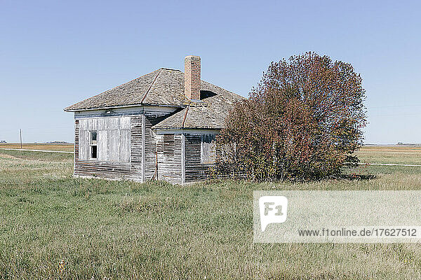 One room school house building by a road on the prairie.