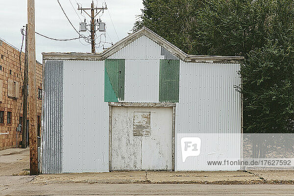 A small metal building boarded up on a sideway in a small town.