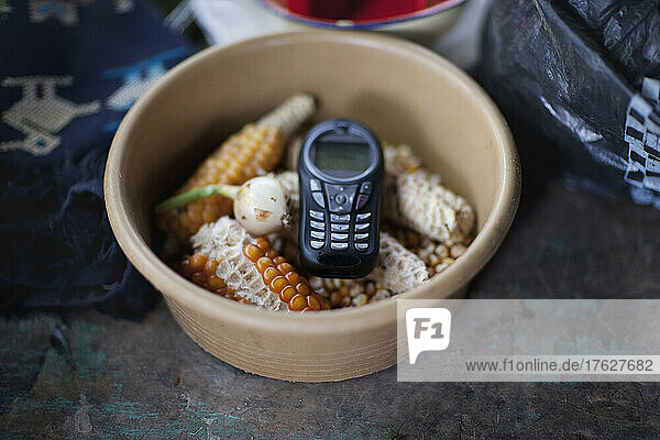 A cell phone mobile communications a handset or telephone in a bowl of maize kernels.