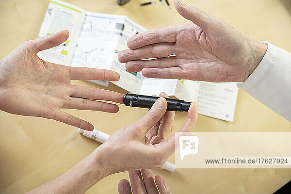 Close-up of a woman's hands and a doctor's hands explaining how to measure her blood sugar and treat her diabetes.