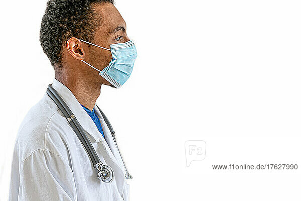 Profile portrait of a young doctor wearing a mask isolated on white background.