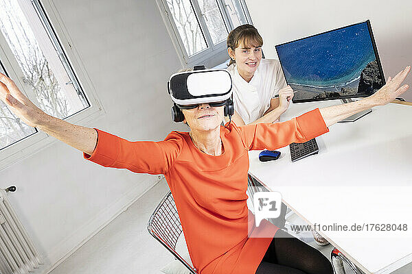Elderly woman  during a therapy session with a virtual reality headset under the supervision of a therapist.