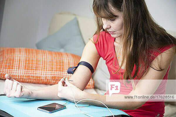 Woman giving herself an injection in her arm from a smartphone.