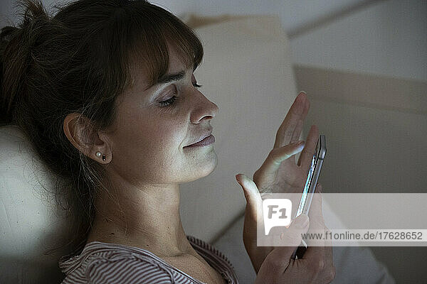 Woman at night admiring her lit smartphone. Addictive behavior.