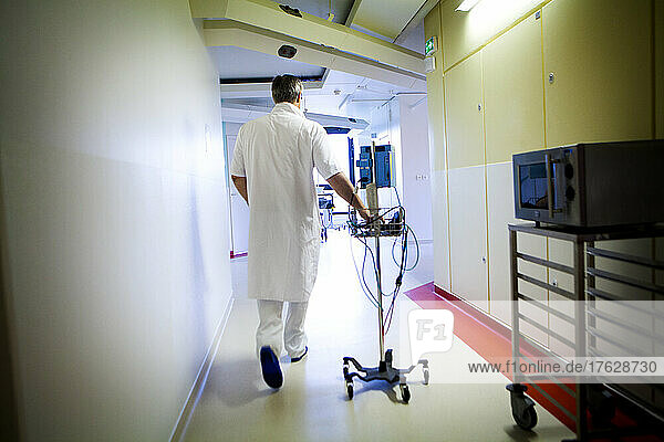Male nurse with electronic blood pressure monitor in a hospital corridor.