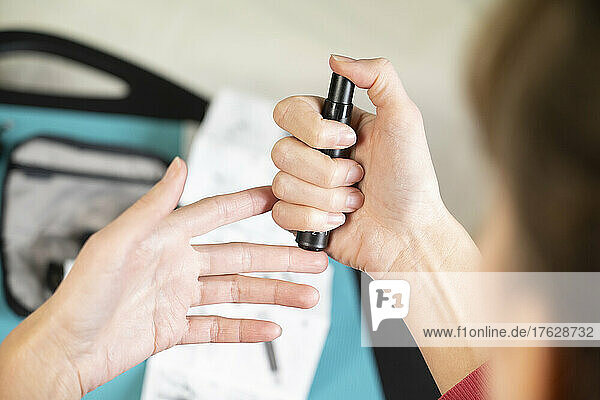 Detail of hands of diabetic woman pricking her finger to measure her blood sugar level.