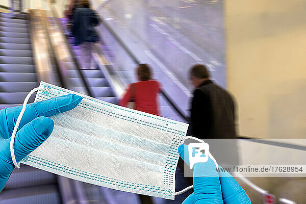 .Hand holding mask and wearing for protection from virus or air pollution on supermarket stairs background