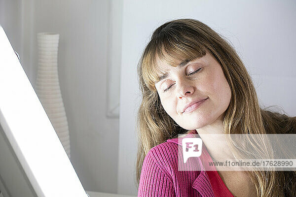 Woman sitting near a white light lamp for light therapy.