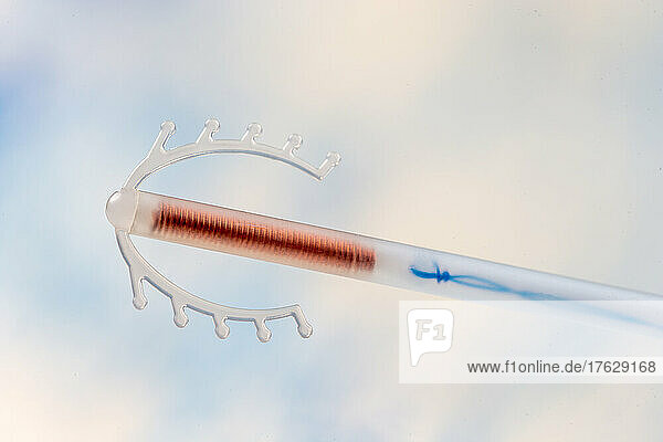 Close up of a copper IUD stored in a plastic tube isolated on a sky blue background.